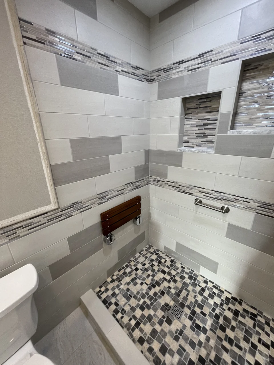 Shower seat and mosaic floor beside tiled walls